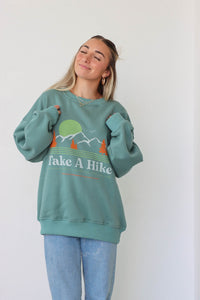 girl wearing "take a hike" green crewneck sweatshirt