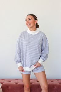 Woman wearing a striped sweater and shorts, standing against a plain background