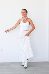 Woman wearing a white outfit with a necklace against a white wall