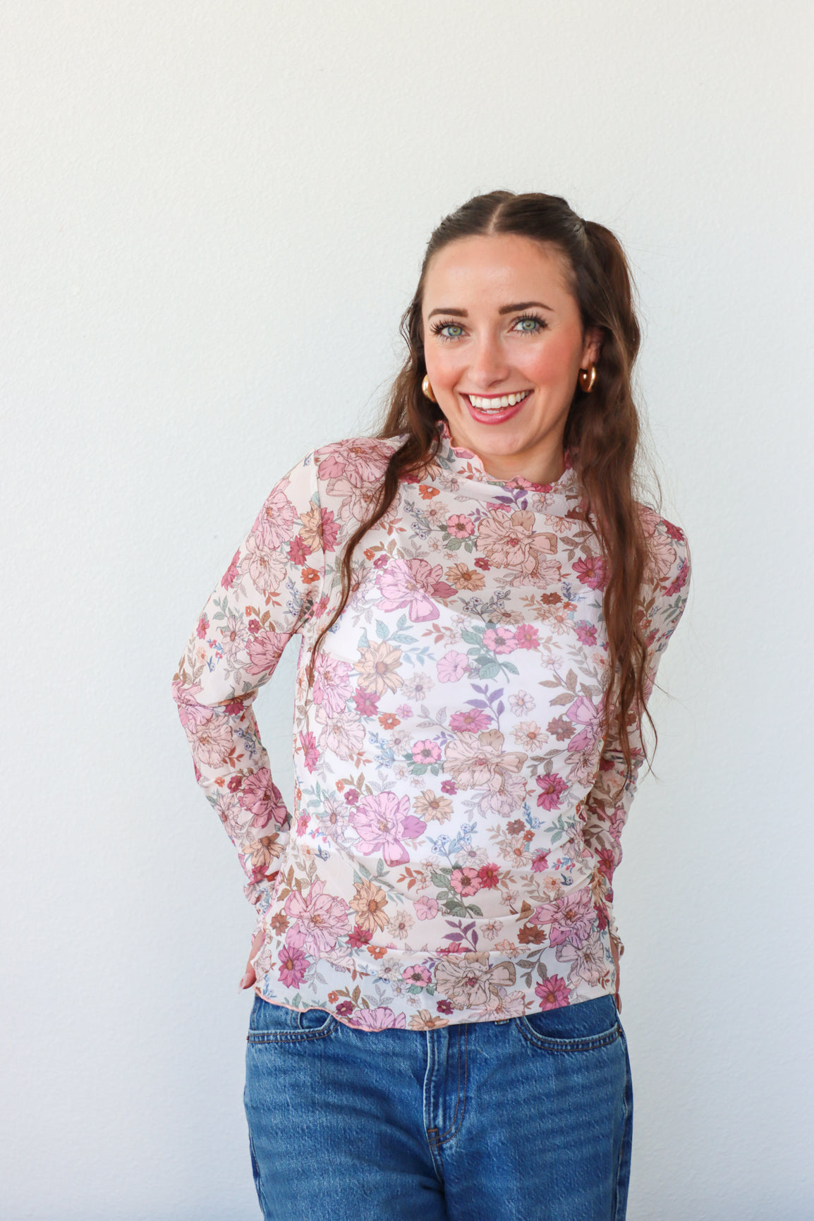 Woman wearing a floral blouse and blue jeans against a white background