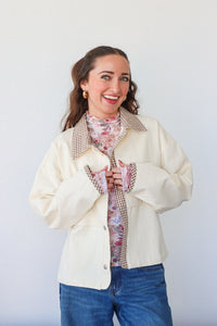 Woman wearing a cream jacket over a floral shirt with a white background