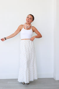 Woman wearing a white top and lace skirt against a white wall