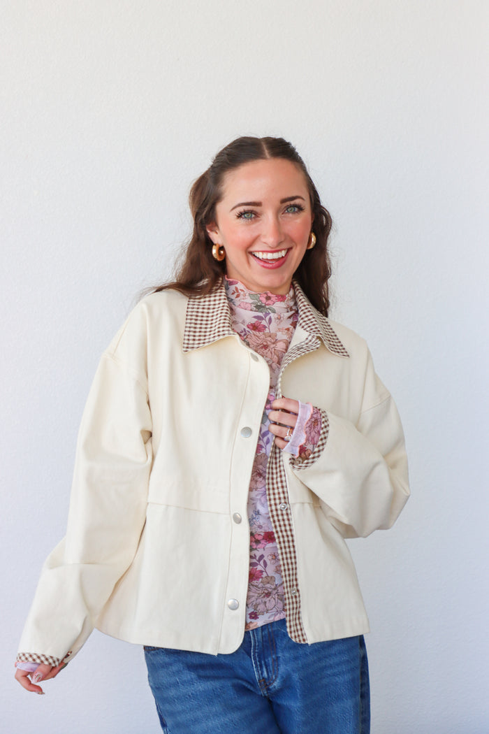 Woman wearing a cream puffer jacket over a plaid shirt with a white background