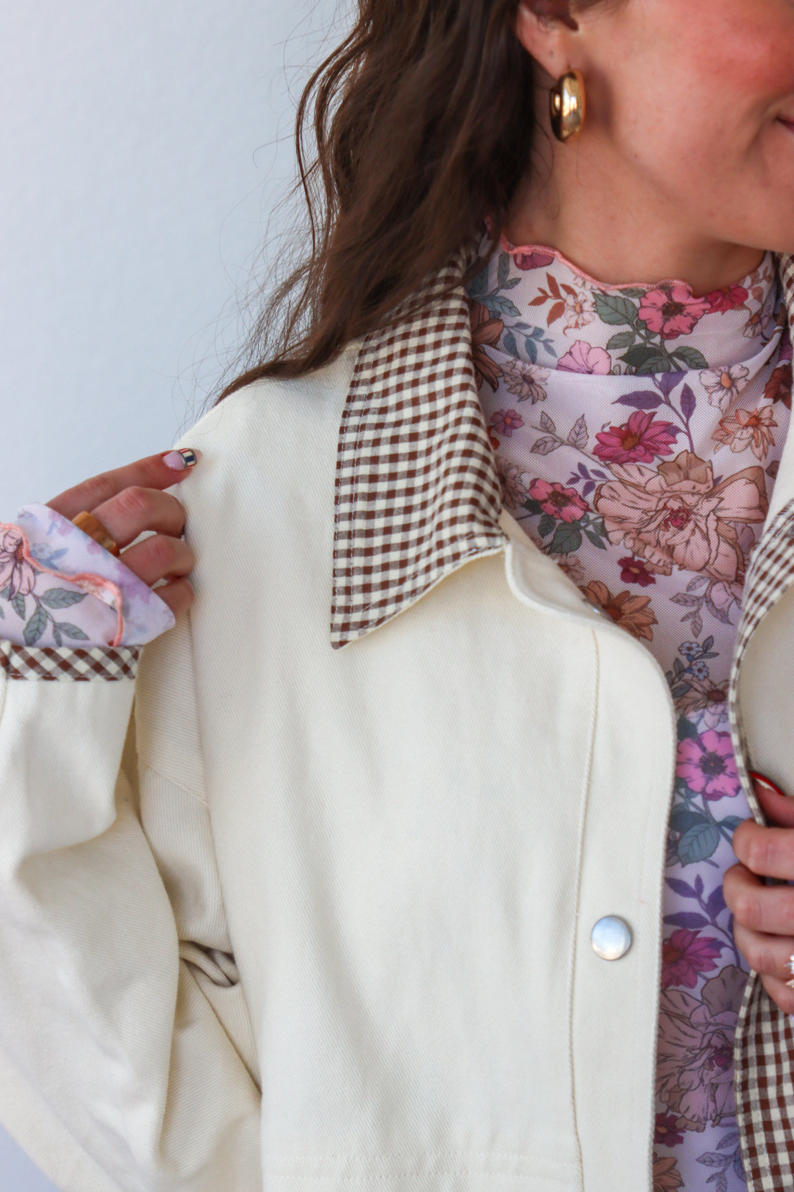 Person wearing a cream jacket with a checkered collar and a floral dress.