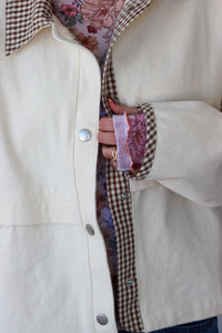 Close-up of a person wearing a cream-colored coat with plaid lining and floral patterned fabric peeking out.