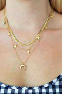 Close-up of a person wearing gold necklaces with star and moon pendants.