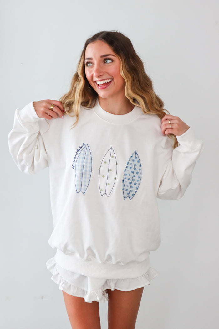 Woman wearing a white sweatshirt with leaf designs on a plain background