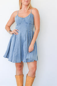 Woman wearing a light blue denim dress with brown boots against a white background