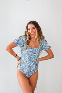 Woman wearing a blue floral one-piece swimsuit on a white background
