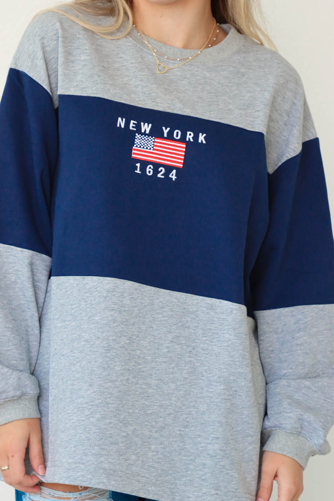 girl wearing gray and navy blue long sleeve shirt with "New York" embroidered graphic