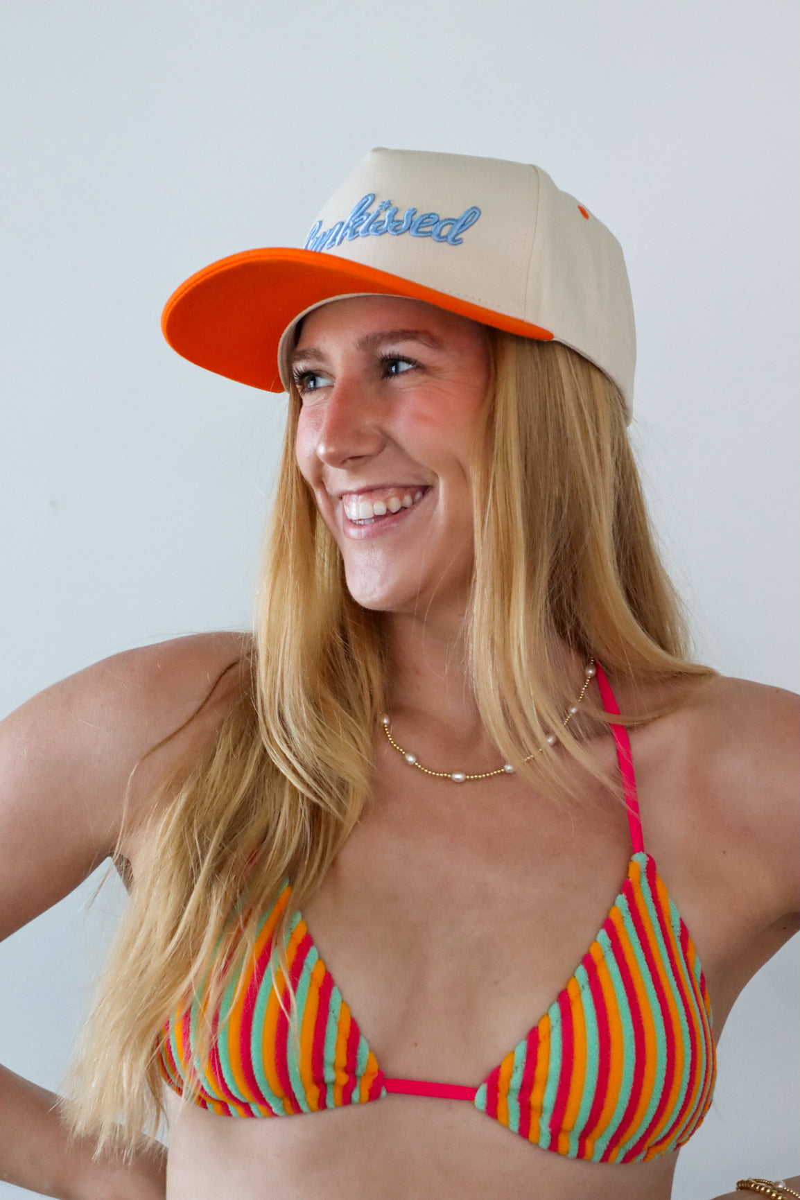 Woman wearing a colorful striped bikini and orange and beige cap against a plain background