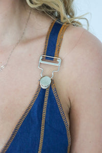 Close-up of a blue halter top with brown trim and metal buckle on a person.