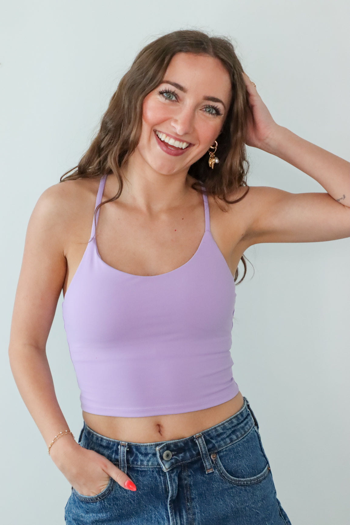 Woman wearing a purple tank top and blue jeans against a plain background