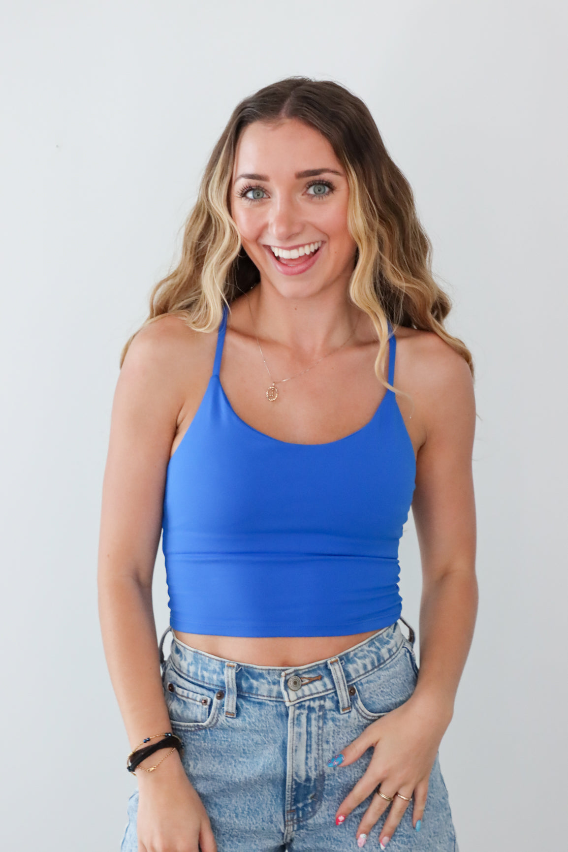 Woman wearing a blue tank top and jeans against a plain background