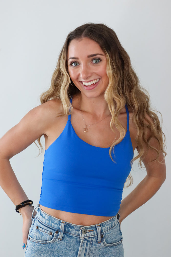 Woman wearing a blue tank top and jeans against a plain background