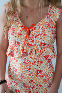Woman wearing a floral dress with orange accents on a plain background