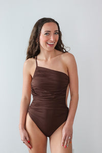 Woman wearing a brown one-piece swimsuit against a light gray background