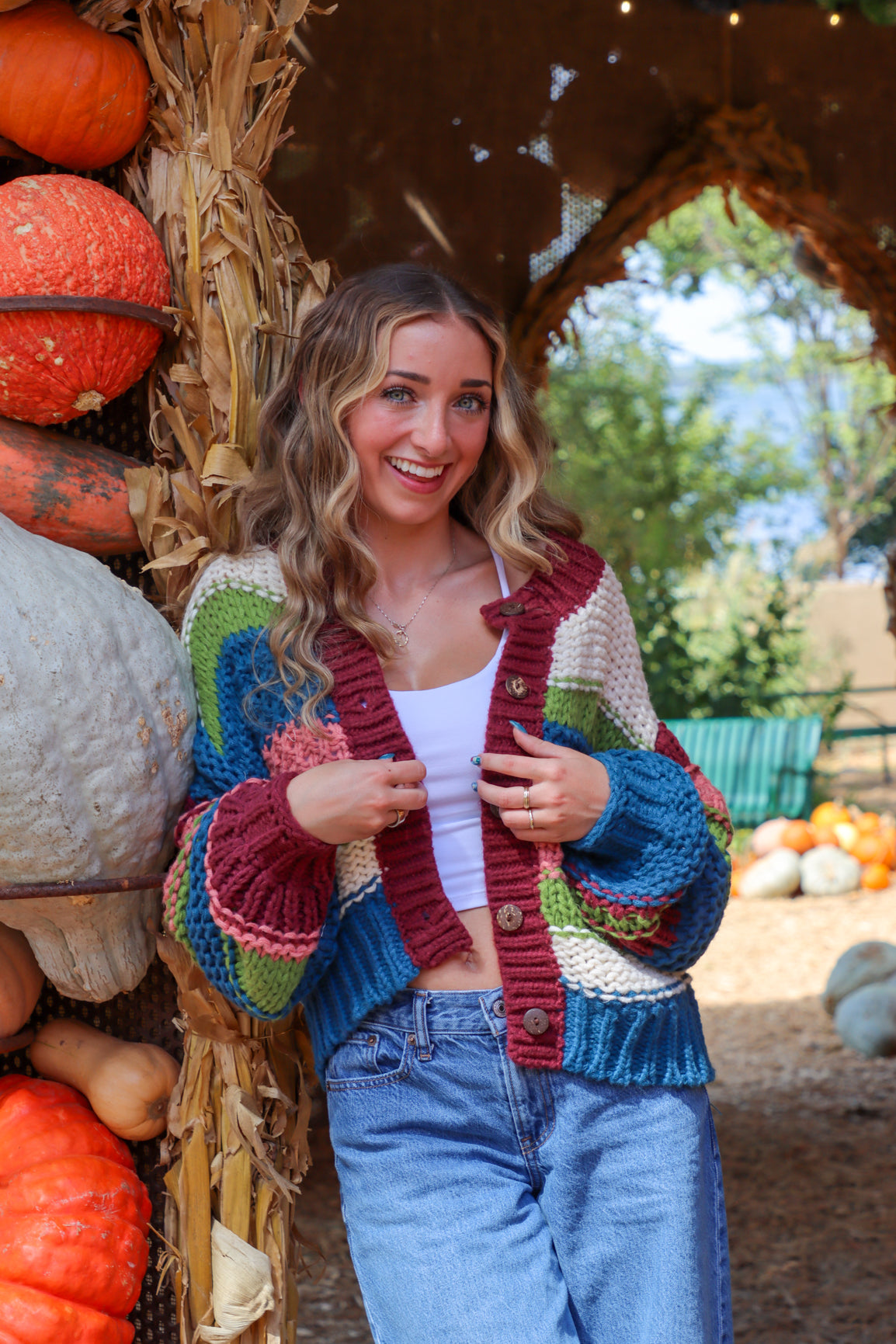 Woman standing in a pumpkin patch wearing a colorful cardigan.