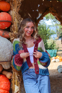 Woman standing in a pumpkin patch wearing a colorful cardigan.