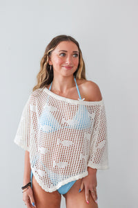 Woman wearing a white crochet cover-up over a blue bikini against a plain background