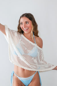Woman wearing a white crochet cover-up and blue bikini against a white background