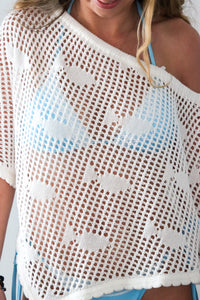 Woman wearing a white crochet cover-up with blue accents.