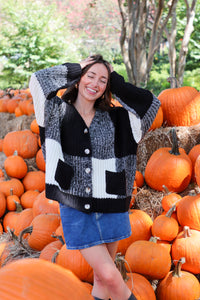 Woman in a patterned cardigan standing among pumpkins in an outdoor setting