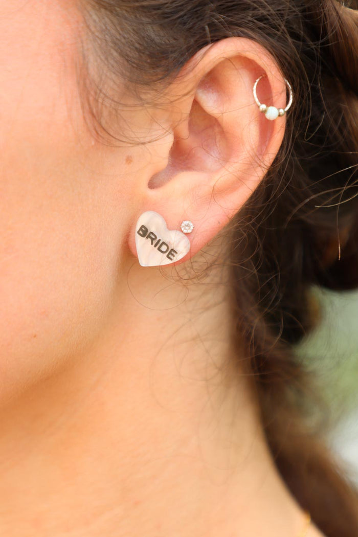 girl wearing white stud heart earrings with "bride" letters