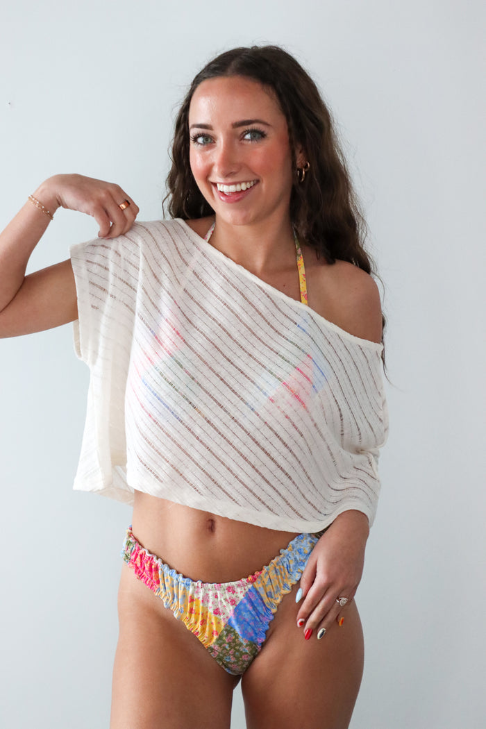 Woman wearing a colorful bikini with a white cover-up against a plain background