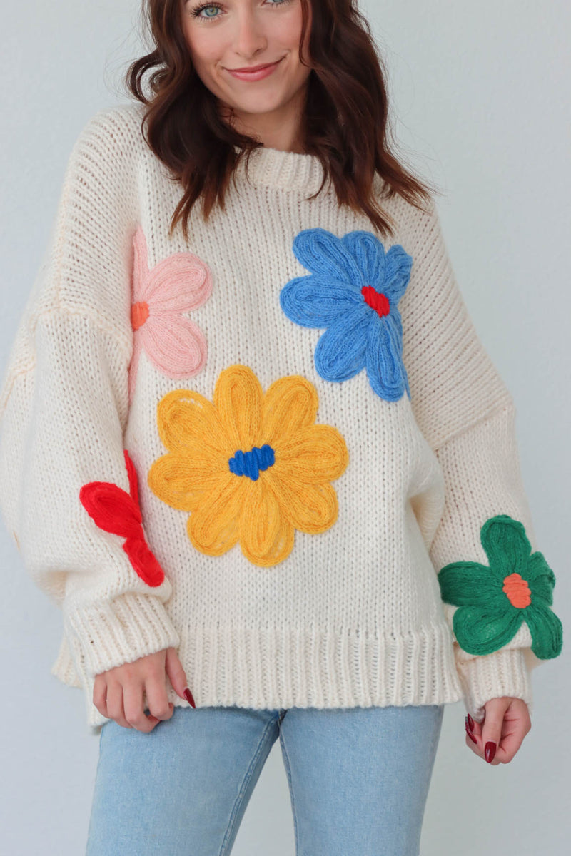 girl wearing cream sweater with large colorful embroidered flower detailing