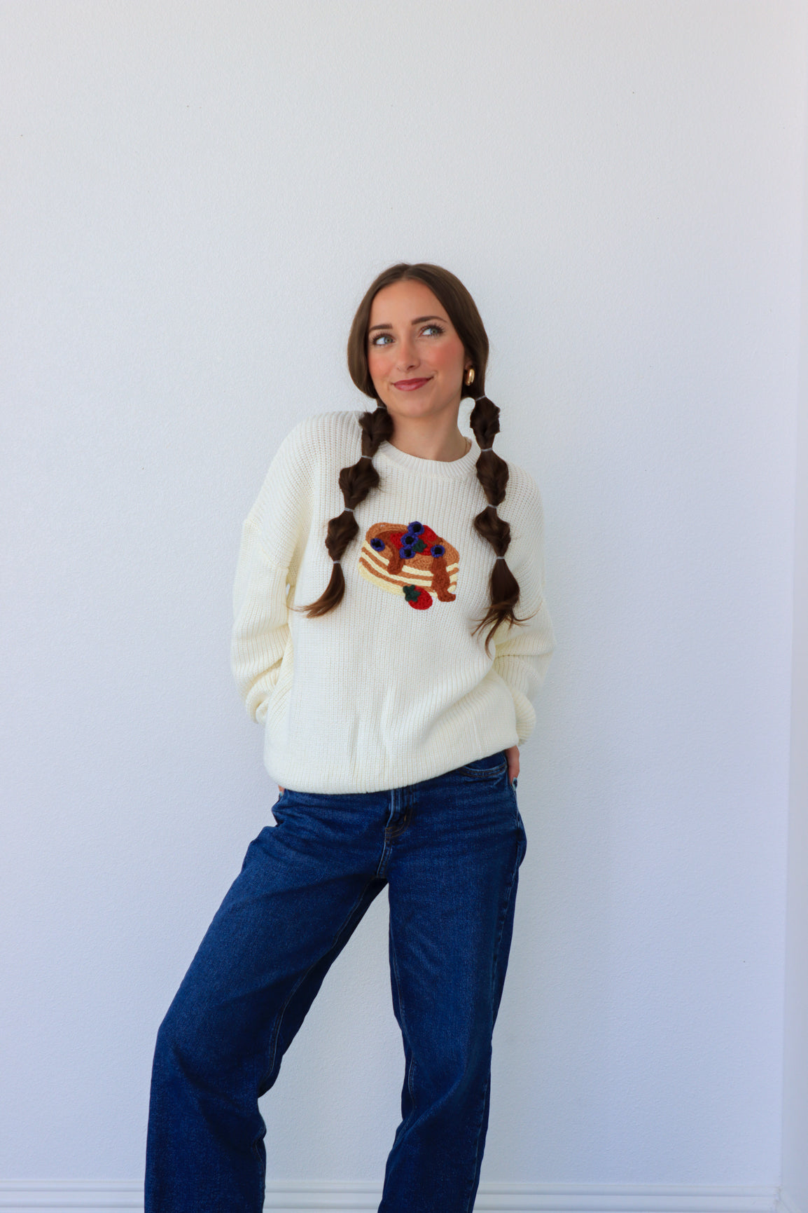 Woman wearing a white sweater with a colorful design and blue jeans against a white background