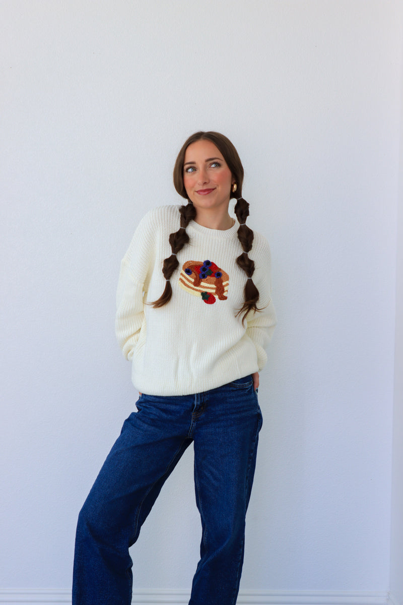 Woman wearing a white sweater with a colorful design and blue jeans against a white background
