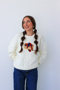 Woman wearing a white sweater with a colorful design, standing against a plain background