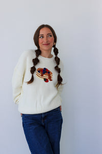 Woman wearing a white sweater with a colorful design, standing against a plain background