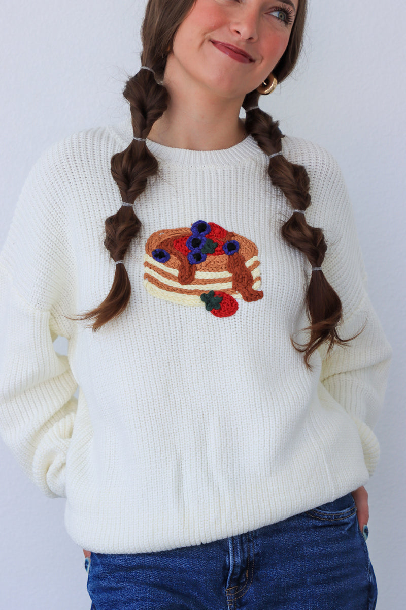 Person wearing a white sweater with a colorful design, standing against a plain background