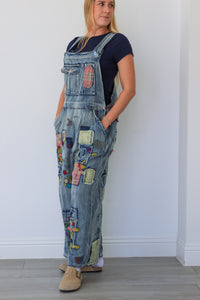 Person wearing a patchwork denim overalls against a white wall.