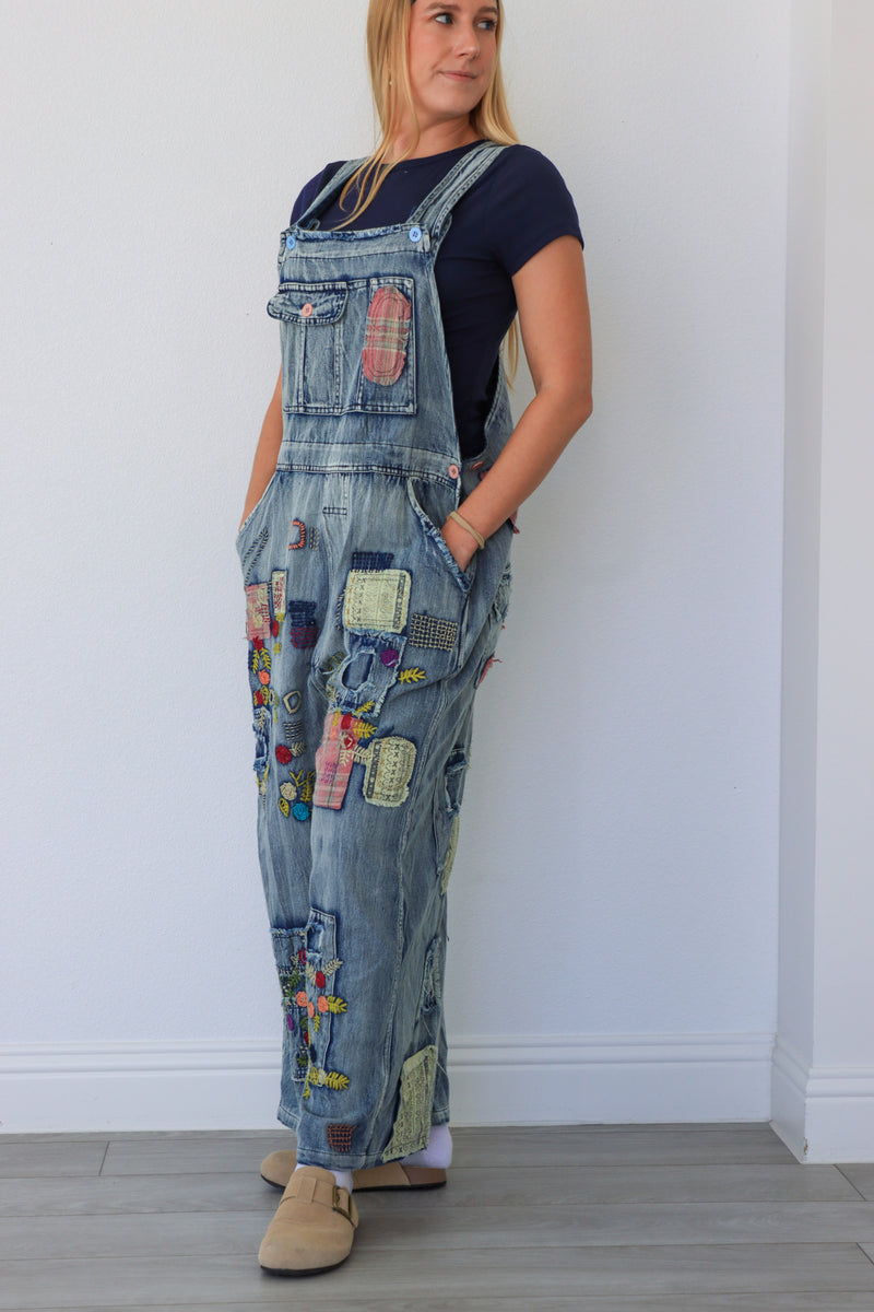 Person wearing a patchwork denim overalls against a white wall.