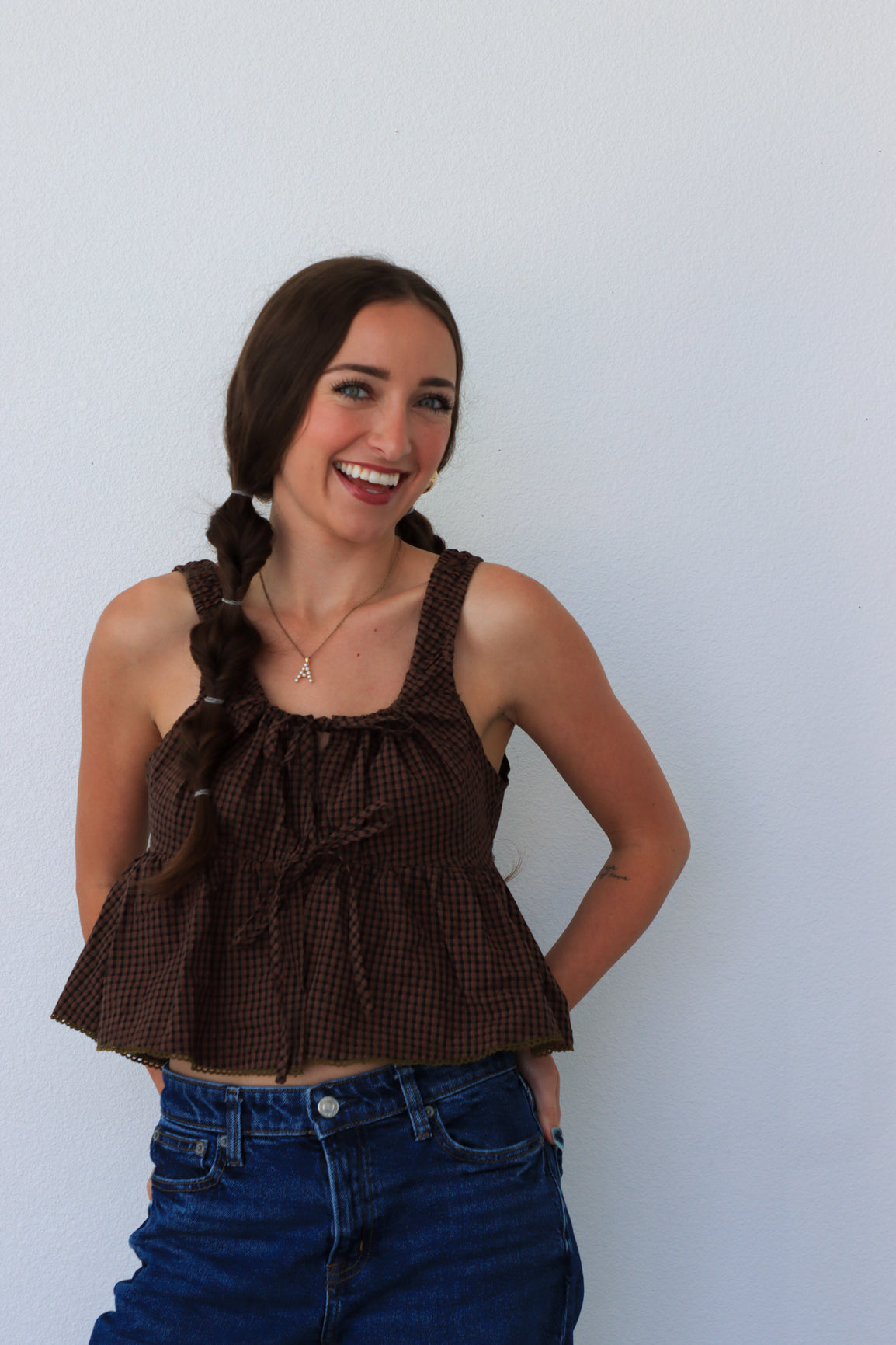 Woman wearing a brown top with ruffled details and blue jeans against a white background