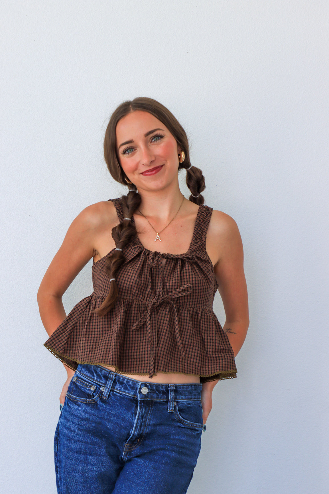 Woman wearing a brown checkered top and blue jeans against a light background