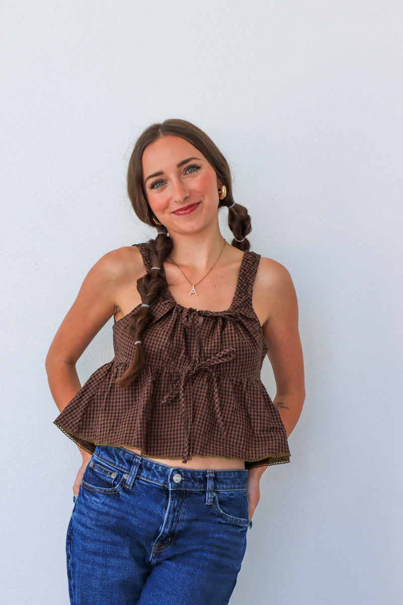 Woman wearing a brown checkered top and blue jeans against a light background