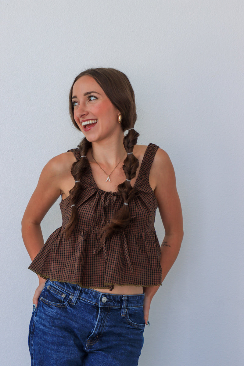Woman wearing a brown checkered top with ruffles against a light gray background