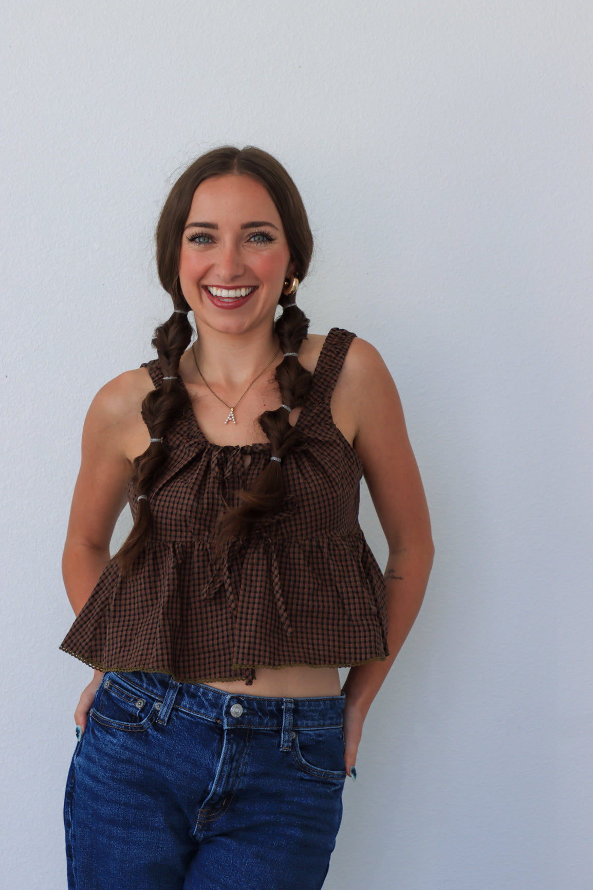 Woman wearing a brown checkered top with ruffles and blue jeans against a white background
