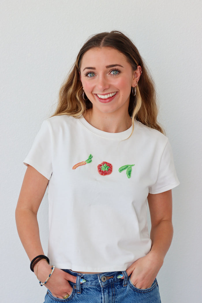 Person wearing a white t-shirt with beaded designs on a plain background