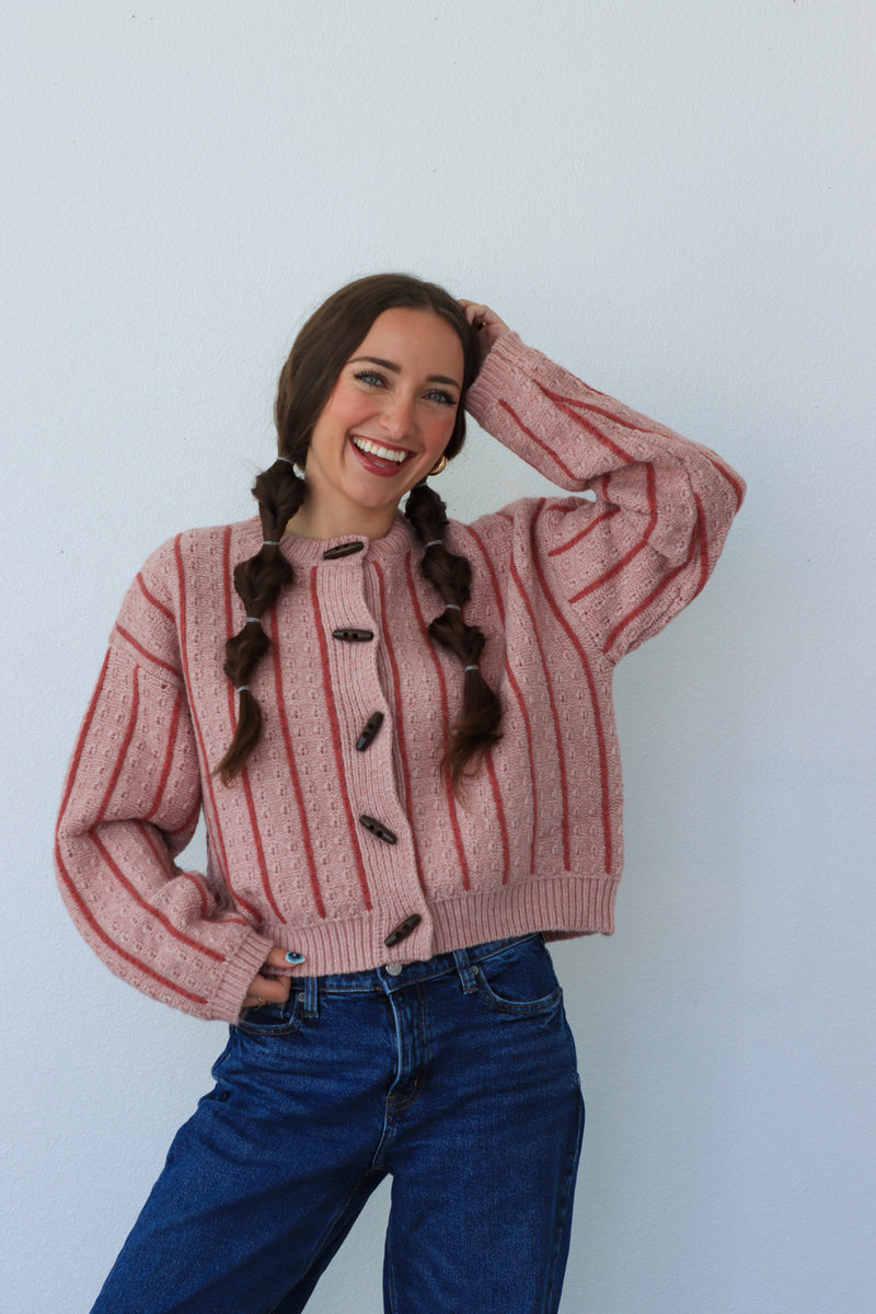 Person wearing a pink striped sweater and blue jeans against a white background