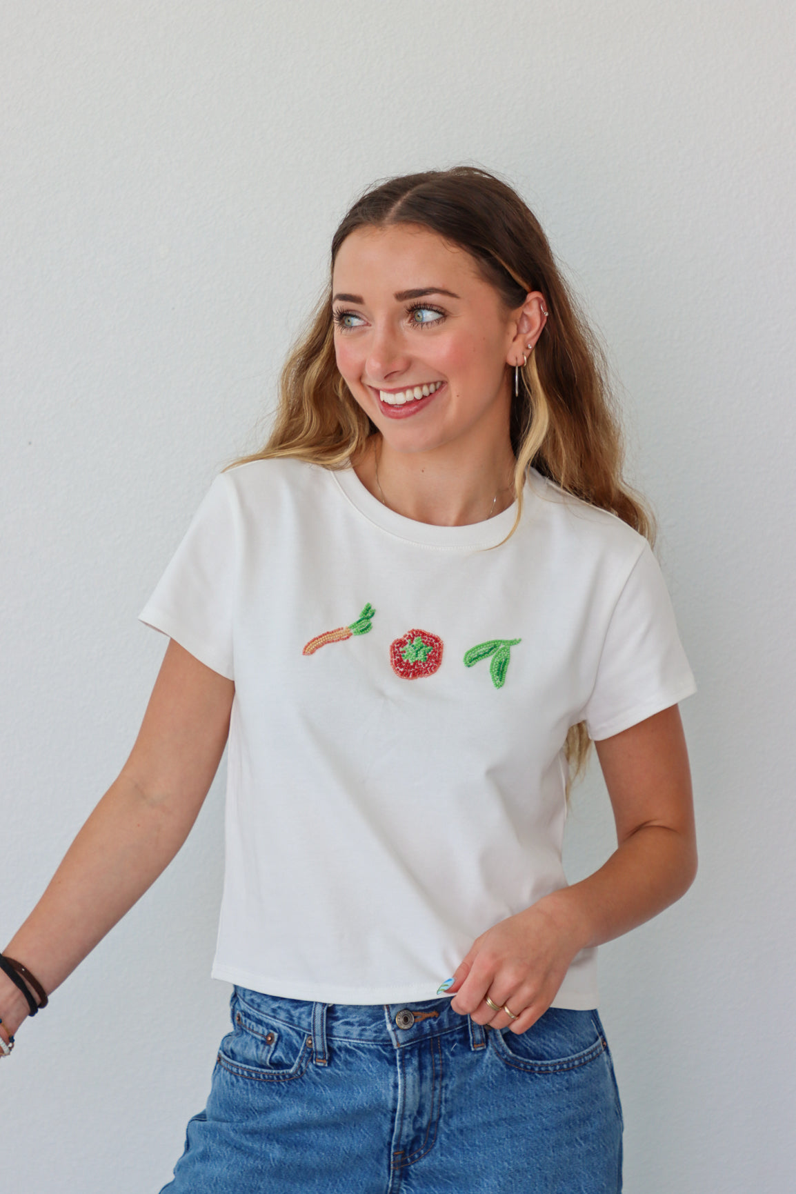 Woman wearing a white t-shirt with beaded vegetables against a plain background