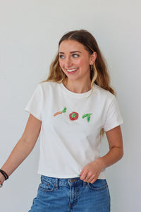 Woman wearing a white t-shirt with beaded vegetables against a plain background