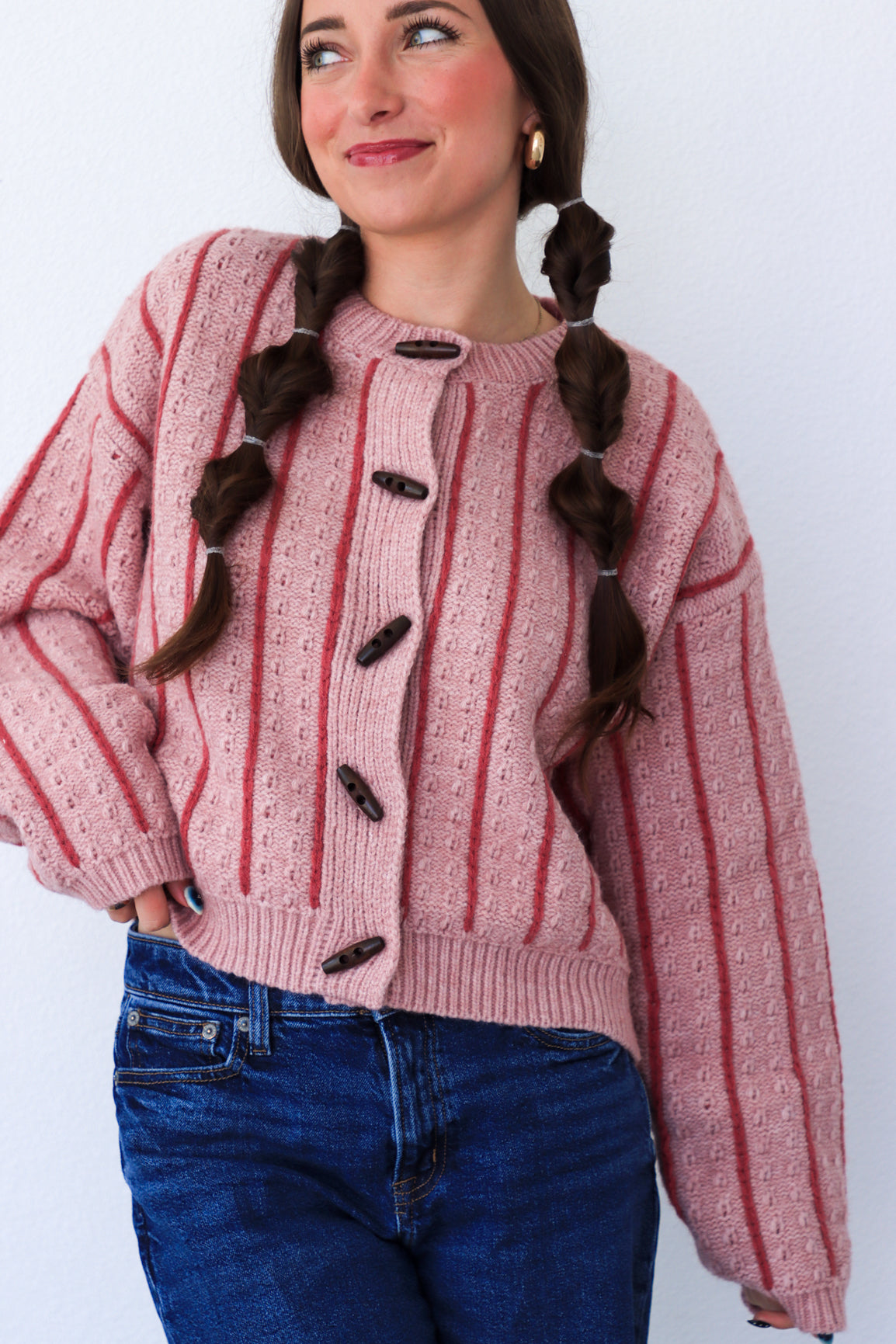 Woman wearing a pink and red striped sweater with black buttons against a white background