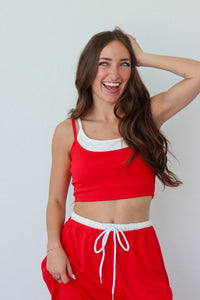 Woman wearing a red tank top and pants with white accents against a plain background