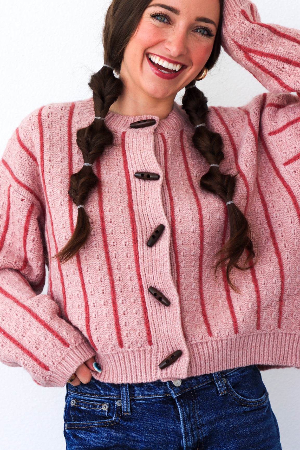 Woman wearing a pink and red striped sweater with buttons, smiling against a white background