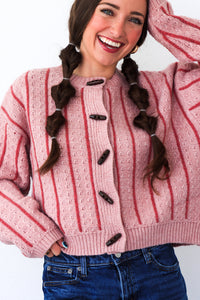 Woman wearing a pink and red striped sweater with buttons, smiling against a white background